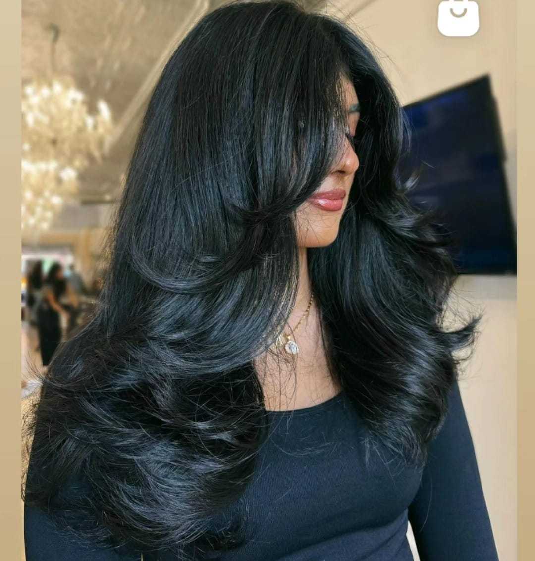 Long layered haircut with voluminous black hair styled in loose waves.