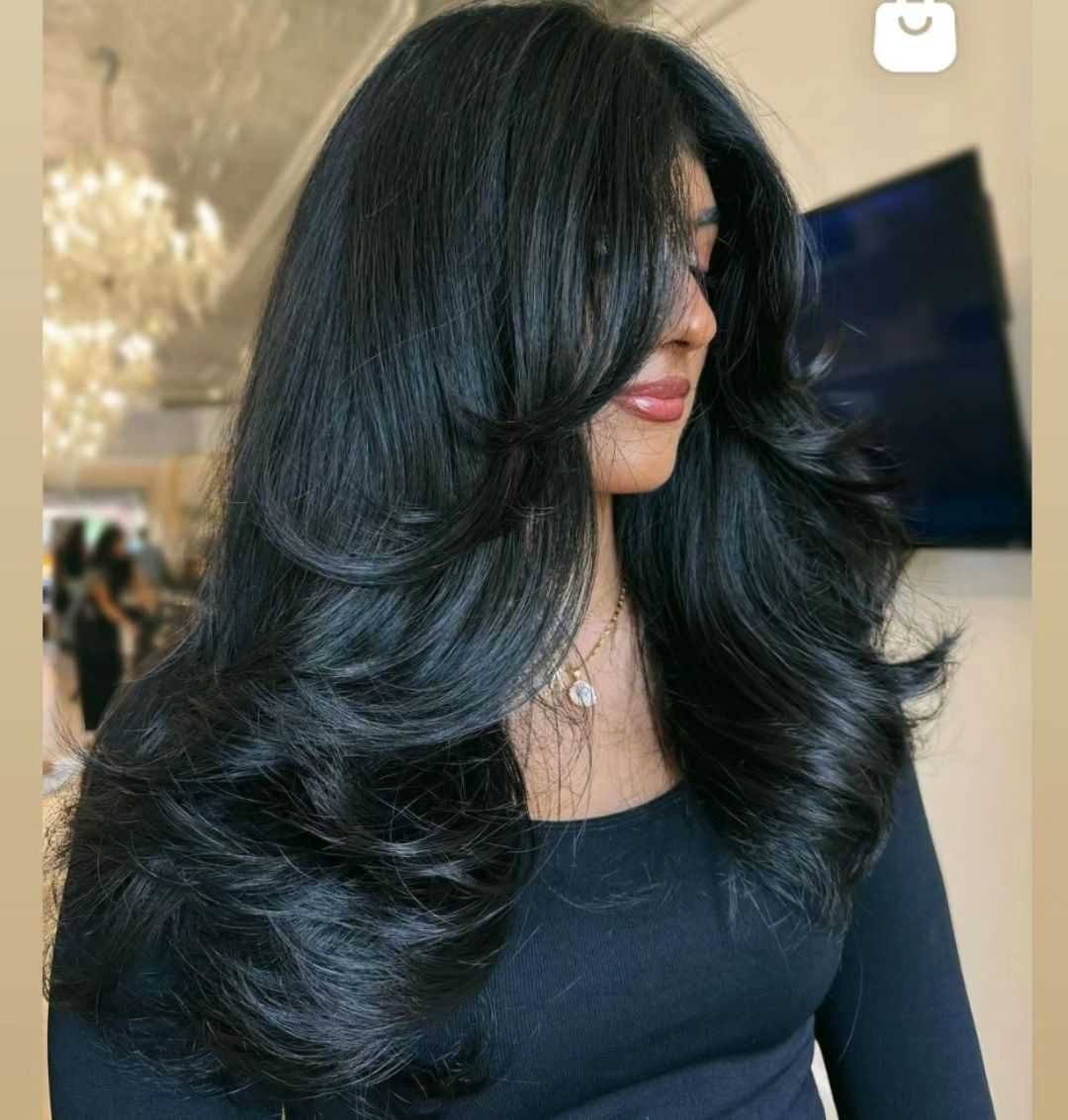 Long layered haircut with voluminous black hair styled in loose waves.