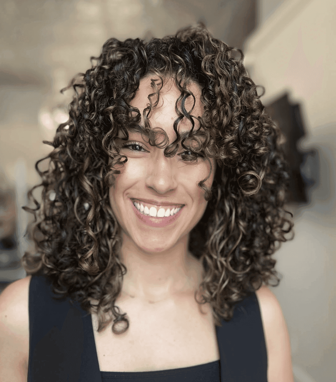 Smiling person with curly hair wearing a sleeveless black top.