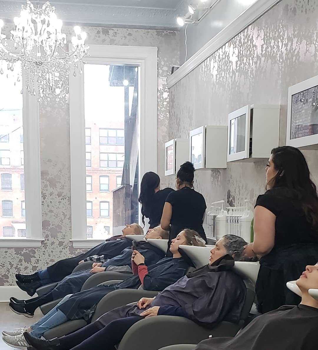 Salon interior with clients receiving hair treatments under a chandelier.