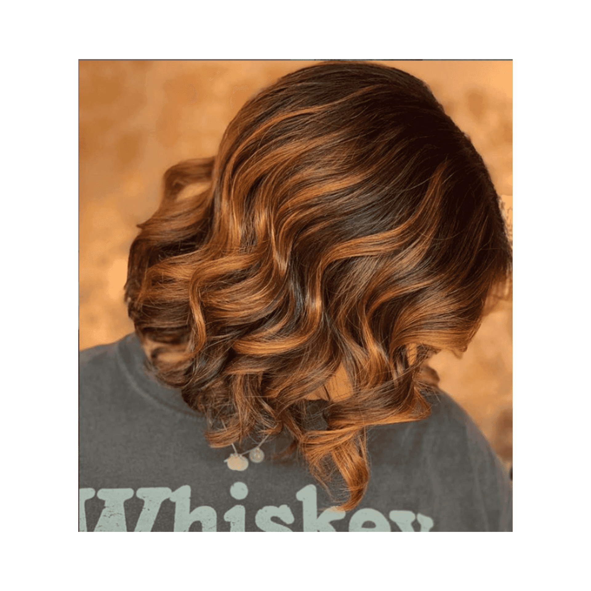 Short brown hair with copper highlights in loose curls against a warm, textured background.
