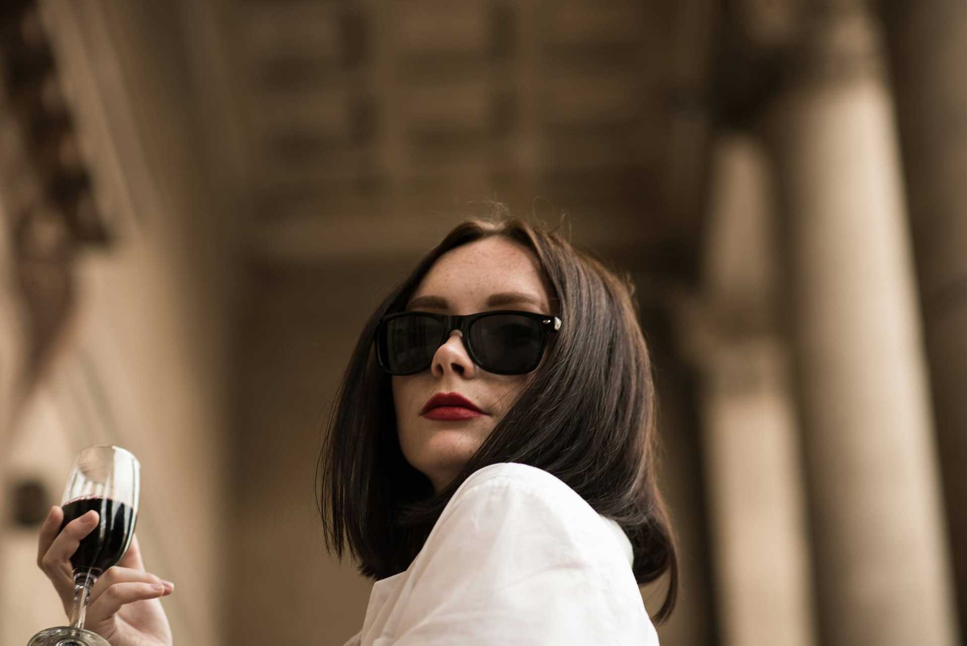 Woman in sunglasses enjoying a glass of wine outdoors in a sophisticated setting.
